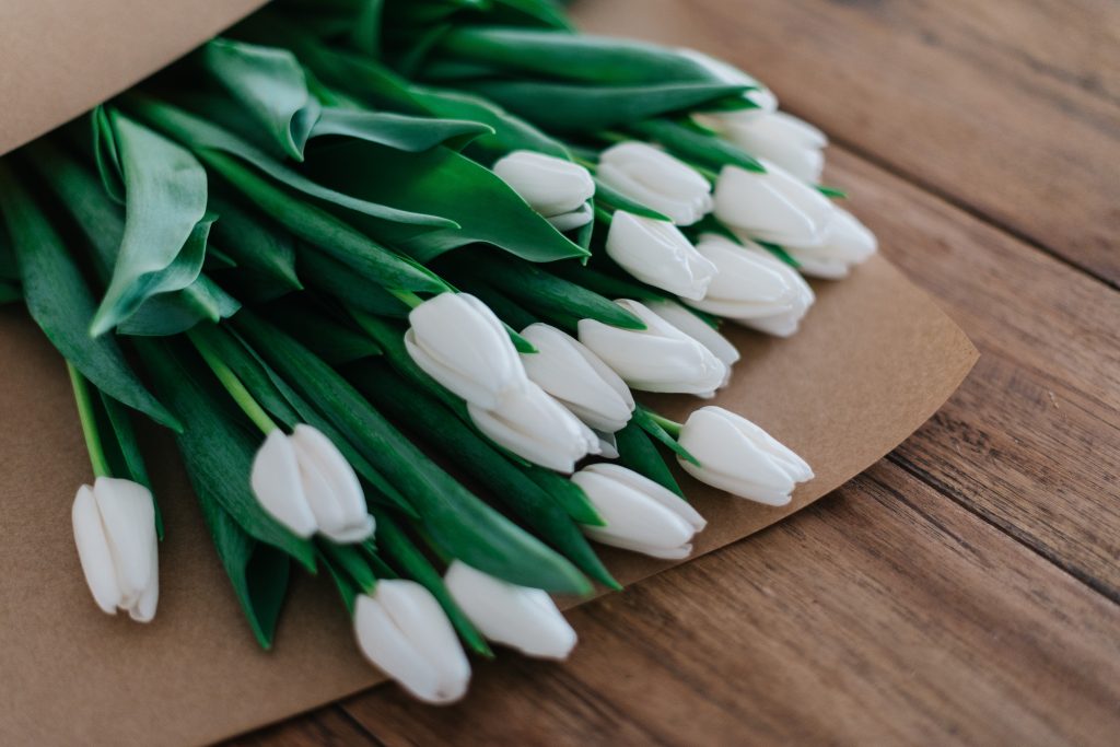Auf einem Holzboden liegt ein Bouquet aus weißen Tulpen