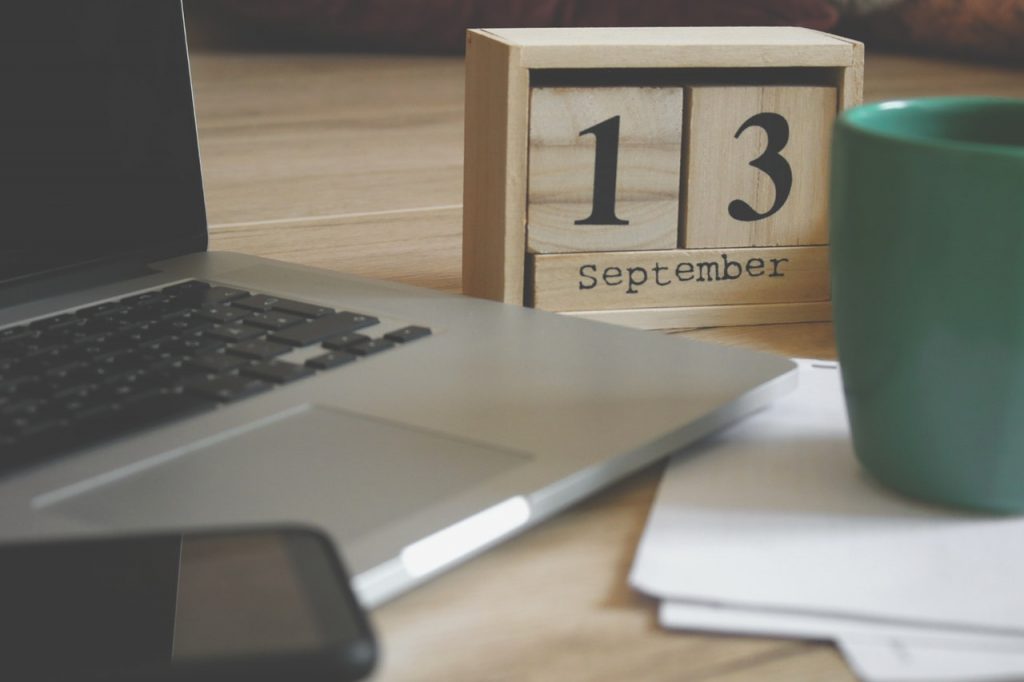 Auf einem Schreibtisch steht ein Laptop eine Tasse und ein Holz-Kalender der jedes Jahr wiederverwendet werden kann