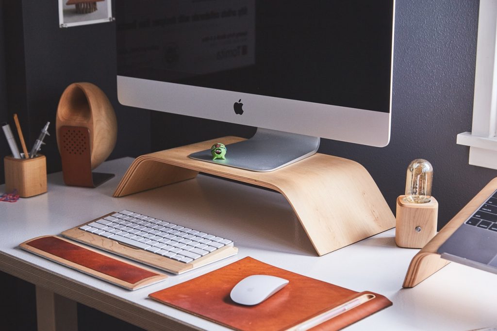 Ein Büroschreibtisch ist mit viel Holz gestaltet: Tastatur, Lampe, Stifthalter und Bildschirmpodest sind aus dem natürlichen Material 