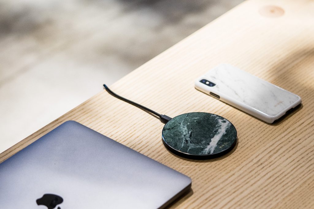 Auf einem Holztisch liegt ein Induktionsladegerät, ein Macbook und ein Smartphone